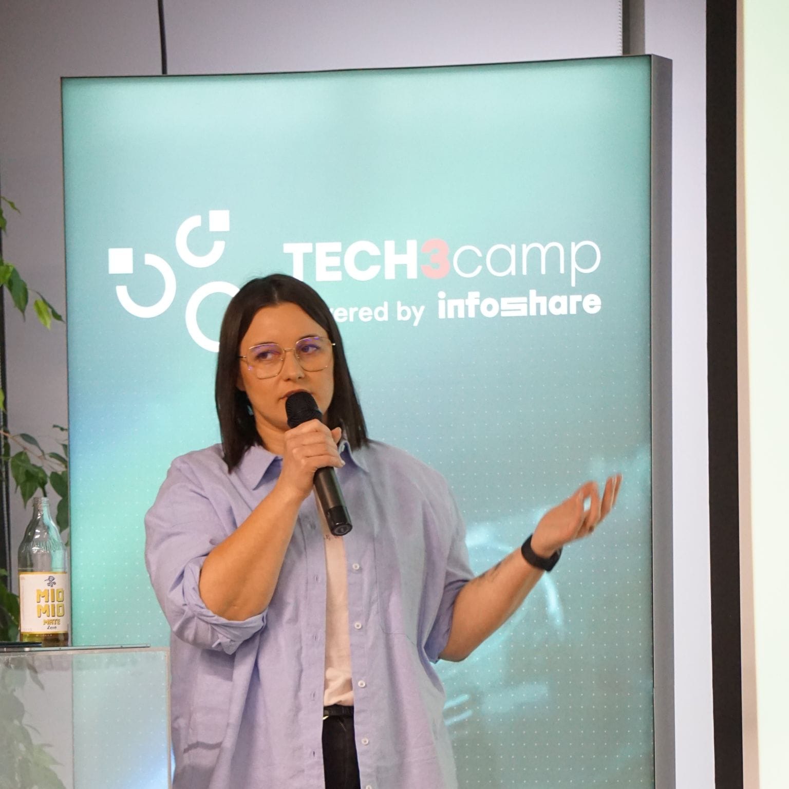 Dominika Bęben mówiąca do mikrofonu na tle banera Tech3Camp.